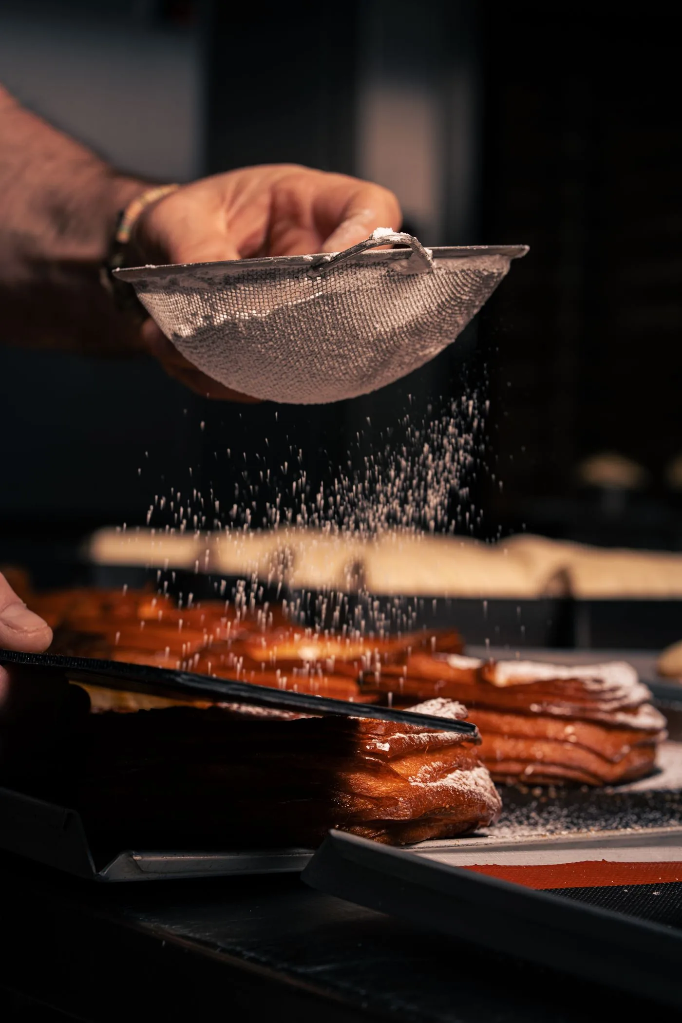 A pastry chef dusting finished éclairs with icing sugar